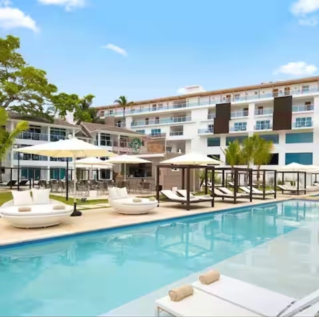 A hotel pool area with sun loungers and umbrellas, surrounded by a multi-story building with balconies.
