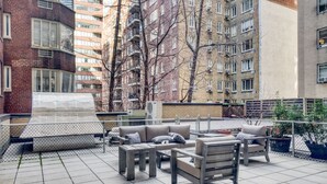 Eine Dachterrasse mit Gartenmöbeln, einem überdachten Sitzbereich und Blick auf die umliegenden Gebäude.