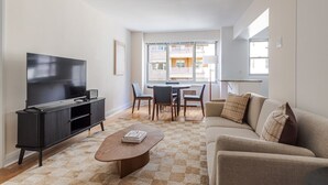 Ein modernes Wohnzimmer mit Flachbildfernseher, dunklem Unterhaltungsschrank, rundem Couchtisch, beiger Couch und Essbereich mit Tisch und Stühlen.
