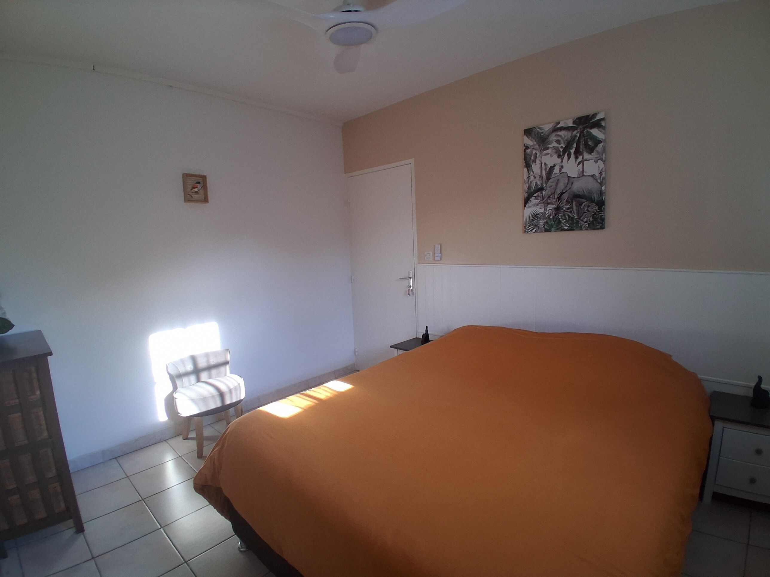 A bedroom with a bed, a chair, a desk, a door, and a ceiling fan.