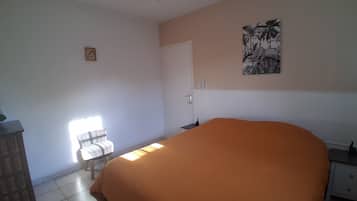 A bedroom with a bed, a chair, a desk, a door, and a ceiling fan.