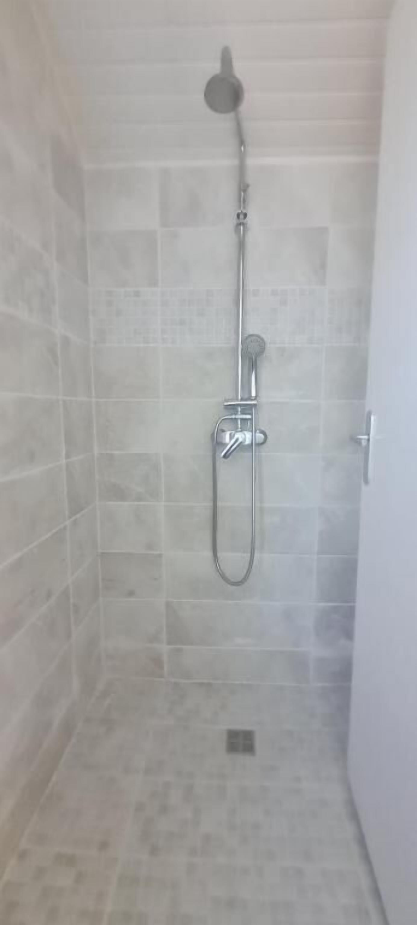 A shower with a handheld showerhead and a wall-mounted faucet.