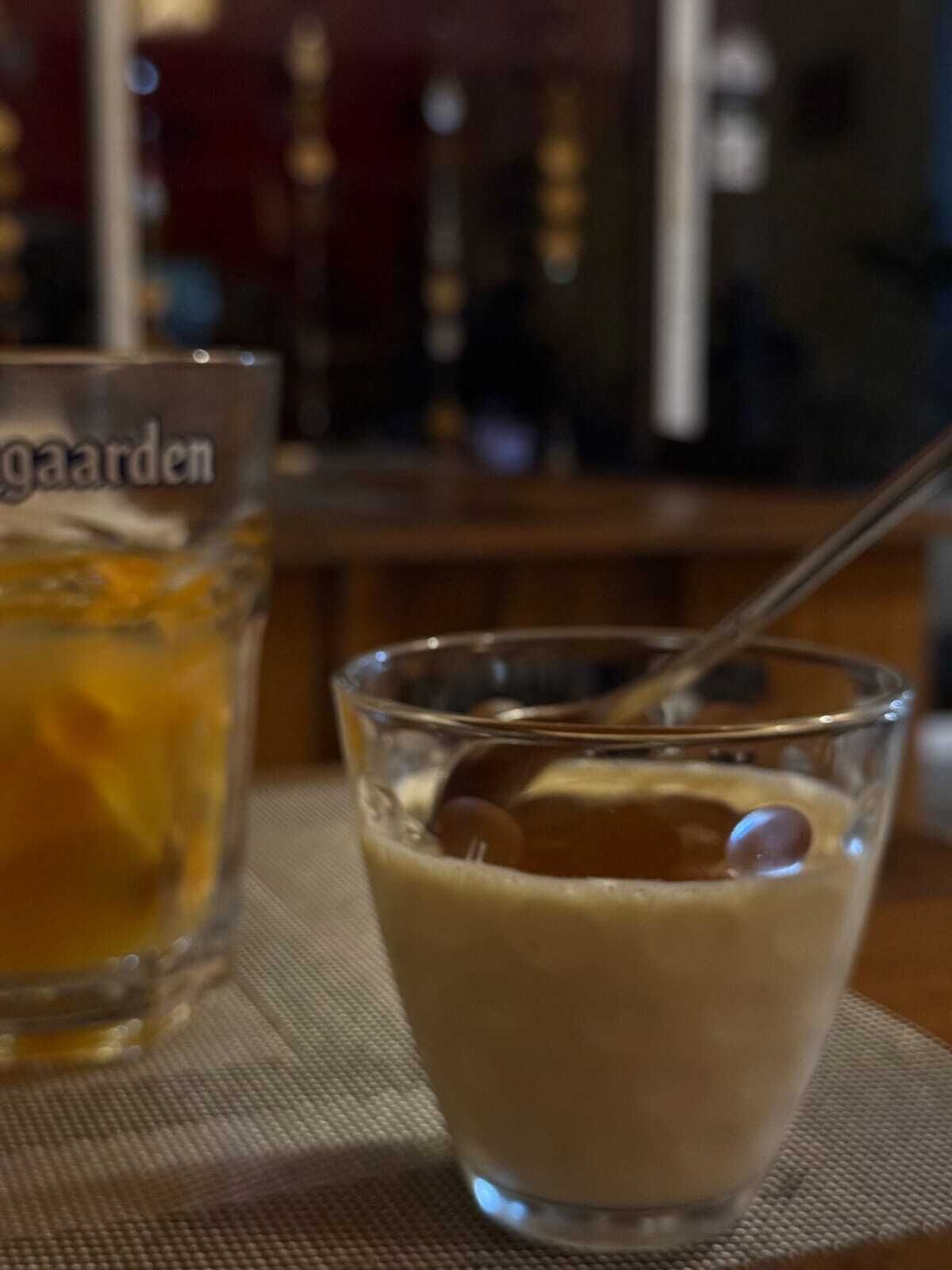 A glass of beer with a straw and a glass of milk with a spoon.