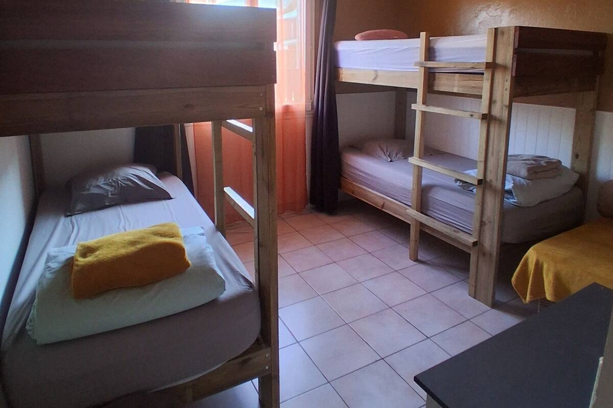 A dormitory room with bunk beds, a ceiling fan, and a window with curtains.