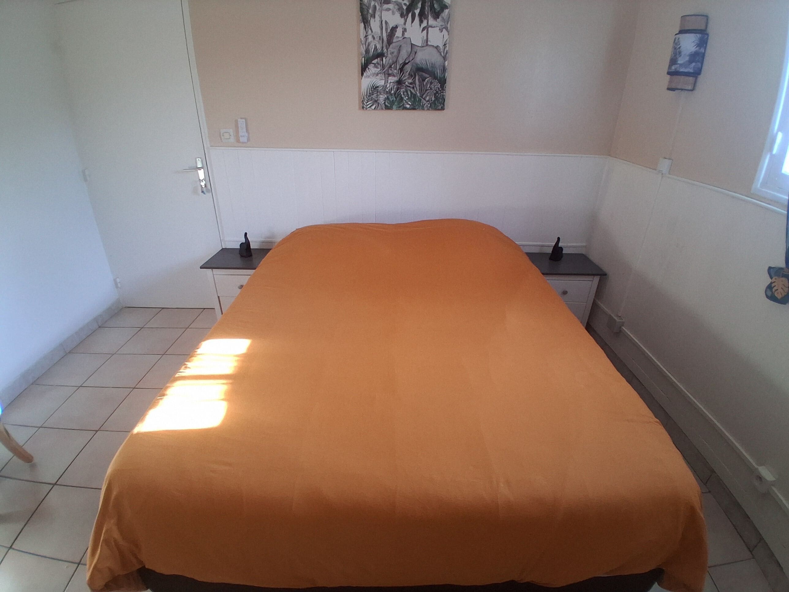 A room with a bed, a nightstand, a wall-mounted light, and a painting.