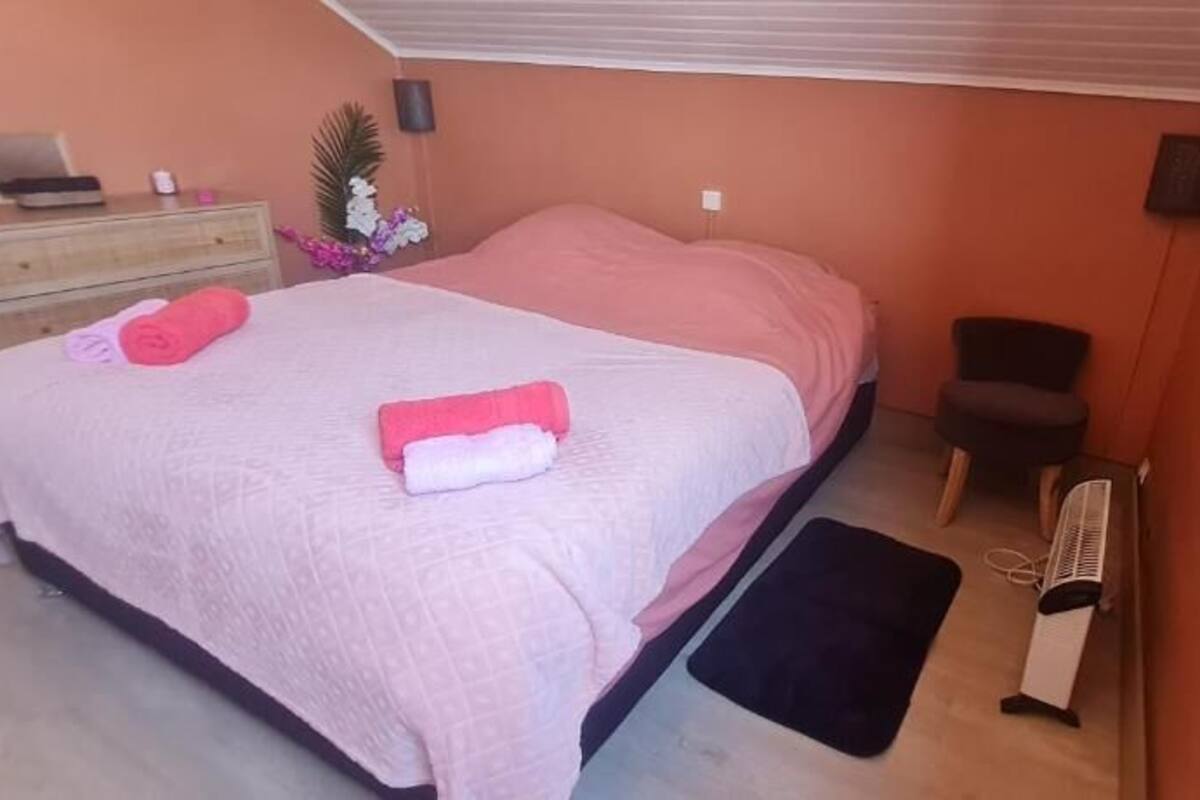 A bedroom with a bed, bedside table, chair, and a small table with a laptop.