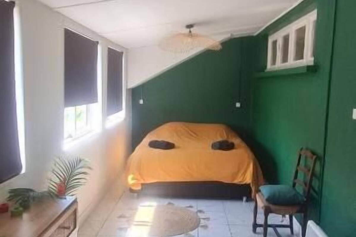 A bedroom with a bed, a dresser, a chair, and a hanging light fixture.