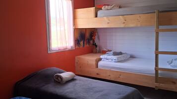 Un dormitorio con dos camas individuales, una litera, una ventana con cortinas y una pequeña mesa con una planta.