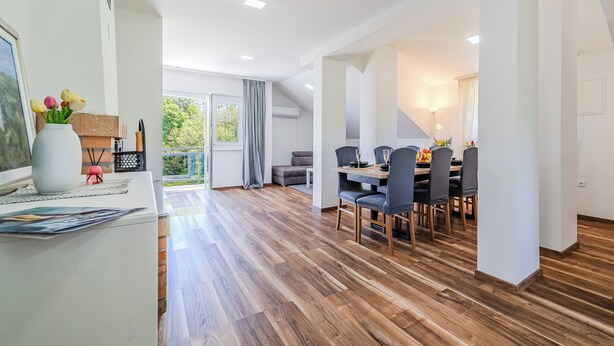 A spacious room with a wooden floor, a dining area with chairs and a table, and a large window with curtains. - The Blue House with Sauna & Jacuzzi, Desinić, Croatia (Desinić)