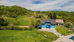 A blue house with a paved driveway, surrounded by green fields and hills. - The Blue House with Sauna & Jacuzzi, Desinić, Croatia (Desinić)