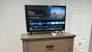 En platt-TV står på en byrå i trä med lådor, en vit dörr syns i bakgrunden och en brandvarnare sitter på väggen.