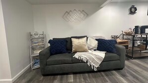 A modern living room with a grey sofa, a white wall, and a wooden floor. - Cozy Home. (Hempstead)