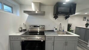 A modern kitchen with stainless steel appliances, grey cabinets, and a built-in microwave. - Cozy Home. (Hempstead)
