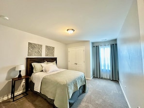 Une chambre à coucher comprenant un lit, une table de chevet, une lampe, des éléments décoratifs sur le mur, une porte et une fenêtre avec des rideaux.