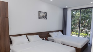 A hotel room with two beds, a wooden wardrobe, a painting on the wall, and a balcony with plants. - Khánh Vy Hotel (Hue)