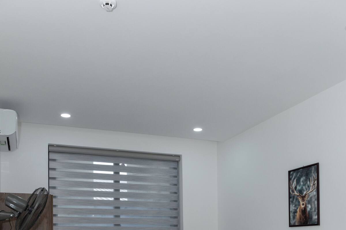 A modern bedroom with a wooden bed frame, a window with blinds, a ceiling fan, and a wall-mounted air conditioner.