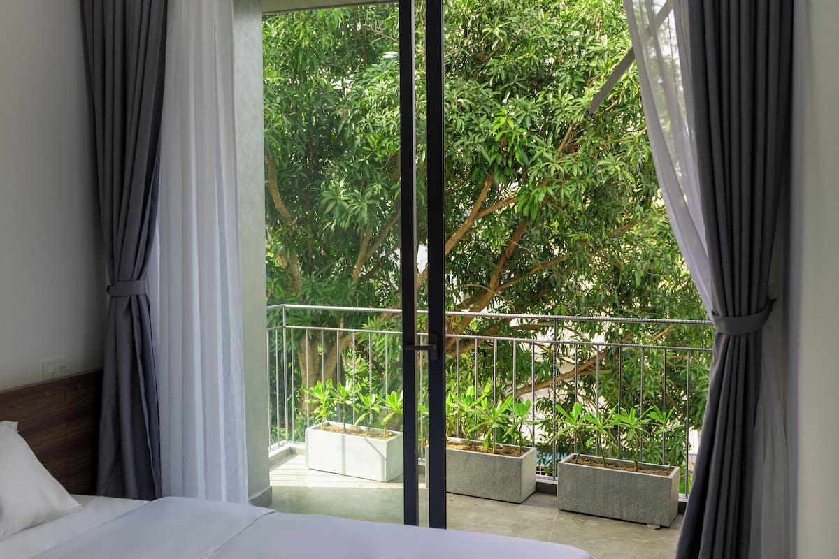 A bedroom with a large window, a bed, and a balcony with potted plants.