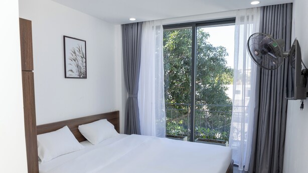 A hotel room with a large bed, a ceiling fan, a window with curtains, and a framed picture on the wall. - Khánh Vy Hotel (Hue)