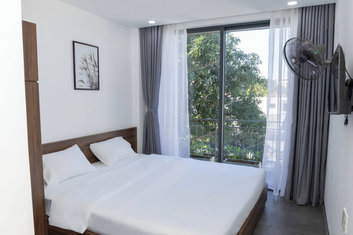 A hotel room with a large bed, a ceiling fan, a window with curtains, and a framed picture on the wall.