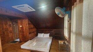 A cozy attic bedroom with a wooden floor, a bed with white linens, a ceiling fan, and a small bedside table with a lamp. - Labah Tong Hill Resort Bandarban (Bandarban)