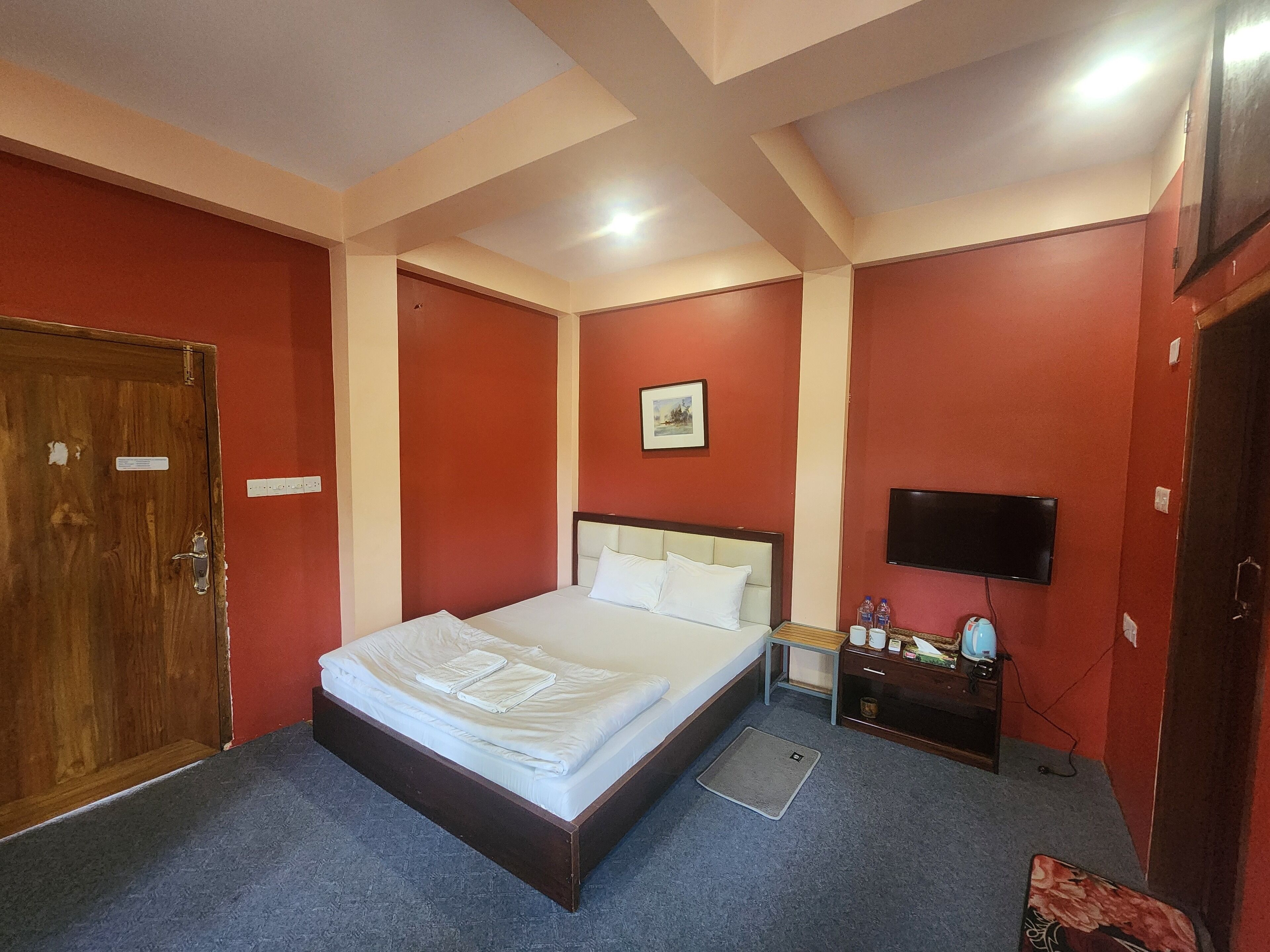 Ein Hotelzimmer mit einem Einzelbett, einem Fernseher, einem kleinen Tisch mit Stuhl und einer Tür.