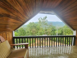 Habitación en ático con techo de madera y vista a una ladera boscosa.