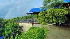 A resort with a covered outdoor seating area, lush greenery, and a visible rainbow. - Labah Tong Hill Resort Bandarban (Bandarban)
