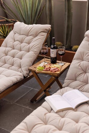 A lounge area with cushioned chairs, a wooden table with a wine bottle and glasses, and a book. - Architectural Condesa Home| Massive Rooftop w/ Gym (Mexico City)