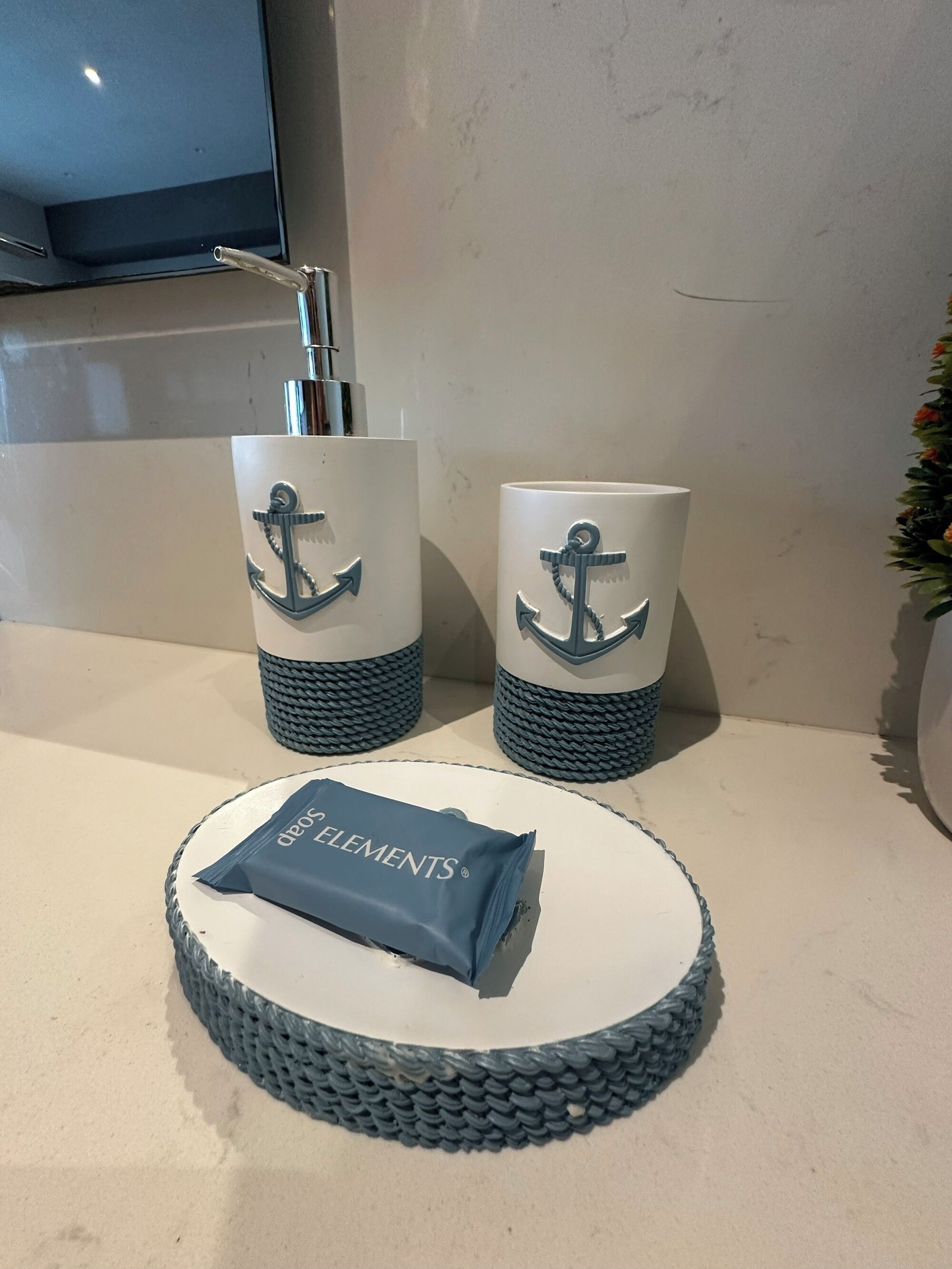 A bathroom counter with two white containers featuring anchor designs, a towel, and a woven basket.