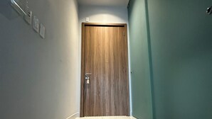Un corridoio con una porta in legno, pavimento piastrellato di colore bianco e pareti chiare.