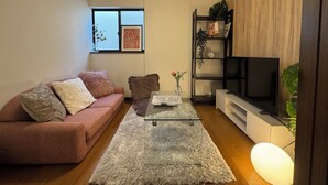Ett vardagsrum med en rosa soffa, ett soffbord i glas, en tv och en bokhylla.