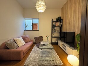 Ein Wohnzimmer mit einem rosafarbenen Sofa, einem Glastisch, einem Fernseher und einem Bücherregal.