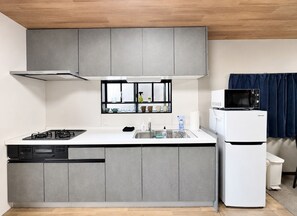 A compact kitchen with grey cabinets, a built-in dishwasher, a microwave, and a stove. - [Tsubame no Ie Imazato] Luxurious Japanese-Modern Entire House Rental | 3 min to Shin-Fukae | 5 min to Imazato | 12 min to Namba by train | Fully renovated in 2026 | Popular with families with children (Oimazato-minami, Higashinari-ku, Osaka-shi)