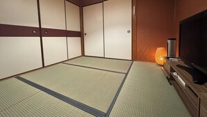 Ett traditionellt japanskt rum med tatamimattor på golvet, skjutdörrar, en tv och en lampa.