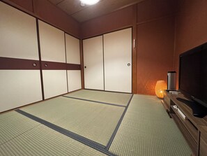 Ein traditioneller japanischer Raum mit Tatami-Boden, Schiebetüren, einem Fernseher und einer Lampe.