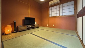 Ett traditionellt japanskt rum med tatamimattor på golvet, en tv på ett träställ, en väggmonterad luftkonditioneringsanläggning och en shoji-skärm.