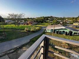 Un camino rural serpentea por un paisaje verde con casas y un pequeño edificio con depósitos.