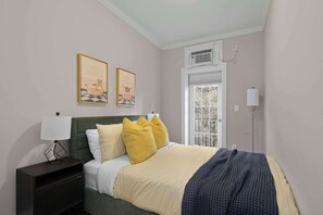 Ein ordentlich eingerichtetes Schlafzimmer mit einem Bett, Kissen, einem Nachttisch mit Lampe und zwei gerahmten Bildern an der Wand.