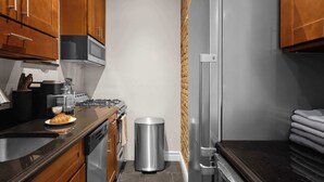 A kitchen with wooden cabinets, a stainless steel trash can, a gas stove, and a refrigerator. - Spacious Midtown Retreat 2BR NYC Haven (New York)