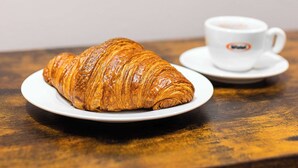 A croissant on a plate with a cup of coffee on a wooden table. - Spacious Midtown Retreat 2BR NYC Haven (New York)
