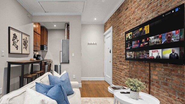 A modern living room with a sofa, a coffee table, and a TV mounted on a brick wall. - Spacious Midtown Retreat 2BR NYC Haven (New York)