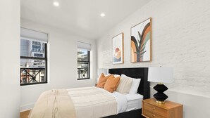 A modern bedroom with a large bed, a nightstand, and two windows. - Prime NYC Location 4BR Spacious Haven (New York)