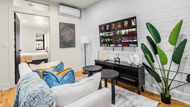 A modern living room with a white couch, a black coffee table, and a large potted plant. - Prime NYC Location 4BR Spacious Haven (New York)