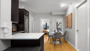 Una cocina moderna con una isla central, un comedor con una mesa redonda y sillas, y un pasillo que conduce a un dormitorio.