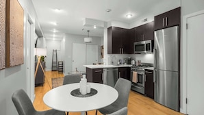 Una cocina moderna con armarios oscuros, electrodomésticos de acero inoxidable y una mesa de comedor redonda con sillas.