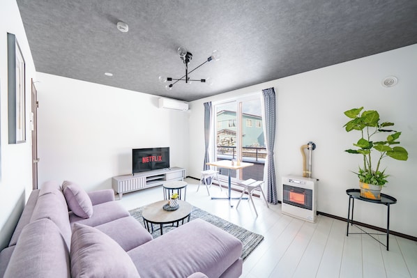 A modern living room with a sofa, a TV, a fireplace, and a balcony with curtains. - HILLS NISEKO 106 (Niseko)