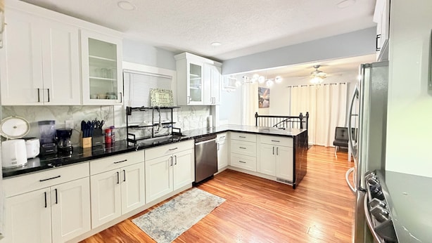 A modern kitchen with white cabinets, a black countertop, and a wooden floor.