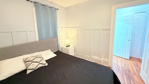 A bedroom with a bed, a nightstand, a lamp, a ceiling fan, and a door.