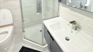 A modern bathroom with a glass-enclosed shower, a white sink with a glass soap dish, and a toilet.
