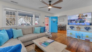 A living room with a gray sofa, a coffee table, and a TV on the wall. - New, Walk to Beach, Game Room, Fire Pit, King Beds (Norfolk)